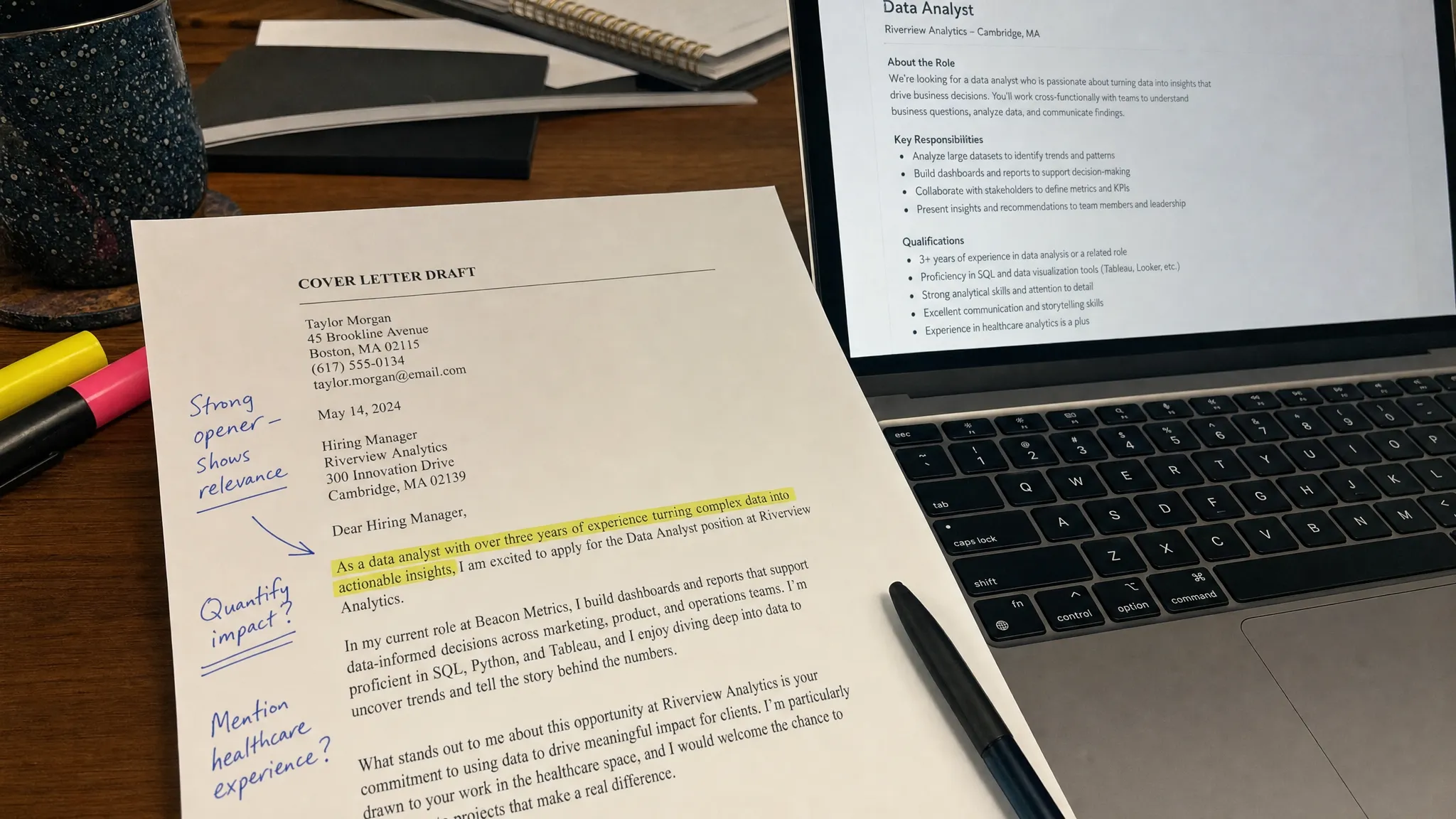 A close-up of a printed cover letter draft on a desk with highlighted first sentences, handwritten notes in the margin, and a laptop nearby showing a job description on the screen facing the writer.